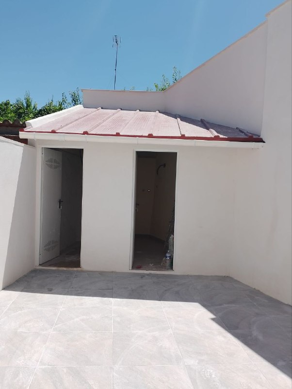 Patio exterior terminado con solado porcelánico moderno, muros blancos y cubierta rehabilitada
