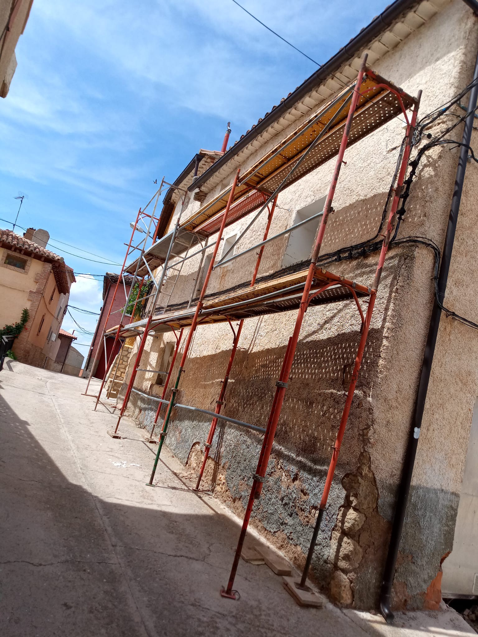 Fachada en obras con andamios tubulares y muro deteriorado antes de rehabilitar